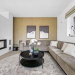 Wohnzimmer mit Ecksofa, Kamin und runden Couchtisch. Wand mit zwei Bildern.