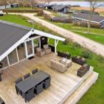 Deck with seating, dining table, and grill. View of green lawn and water.