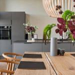 Dining area with wooden table, chairs, and modern kitchen in background.
