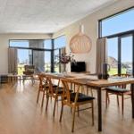 Dining area with wooden table and chairs, large windows, and terrace overlooking green space.