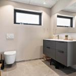 Bathroom with sink, mirror, toilet, and window.