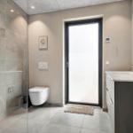 Bathroom with shower, toilet, and sink. Large window and modern design.