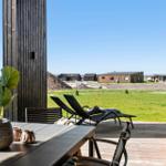 Deck with table, chairs, and lounge chairs. View of grassy area and modern houses in the background.