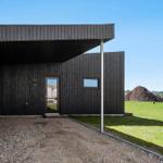 Modern wooden cabin with entrance door and window. Lawn and construction sites in background.