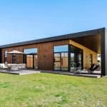 Modern wooden house with large deck and garden. Outdoor seating and lounge chairs.