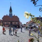 Cobbled street with historic town hall and market stalls. People stroll on stone pavement.