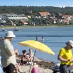 Beach with bathers, yellow umbrella, and view of houses by the water.