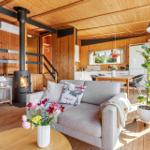Living room with fireplace, sofa, and kitchen area. Wooden floor and ceiling.