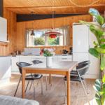 Dining area with wooden table, black chairs, and window view. Kitchen with white cabinets and refrigerator.