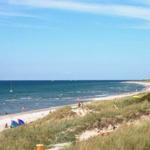 Beach with dunes, beachgoers, and sailboats in the background.