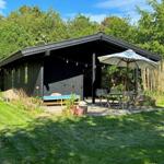 Black wooden house with terrace, sun lounger, and table with chairs under umbrella.