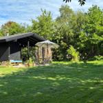Black house with terrace, umbrella, and garden. Surrounded by trees and grass.