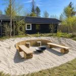 Sandy area with wooden benches, fire pit, and log stools in front of a house.