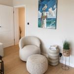 Wohnzimmer mit Sitzgelegenheit, Wandbild und Pflanze. Küchenbereich sichtbar.