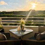 Terrasse mit Tisch und zwei Stühlen, Blick auf Grünflächen und Sonnenuntergang.