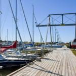 Holzsteg mit Segelbooten und Kränen am Hafen