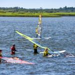 Windsurfer üben im Wasser, einige stehen im Wasser und halten Segel.