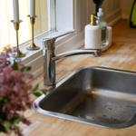 Edler Edelstahl-Spüle mit modernem Wasserhahn auf Holzoberfläche. Zwei Kerzenhalter und Blumen im Vordergrund.