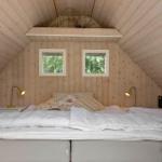 Schlafzimmer mit Holzwand, zwei Fenstern und Bett mit weißen Bettwäsche.