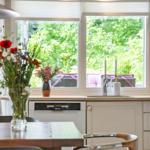 Küche mit Holzwand, Fenster und Tisch. Blumen und Spüle sind sichtbar.