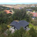 Haus mit Terrasse umgeben von Bäumen, Blick auf Strand und Dünen.