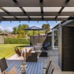 Terrasse mit Pavillon, Tisch, Stühlen, Sonnenschirm und Liegen. Blick auf grünen Garten.