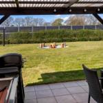 Terrasse mit Grill, Tisch und Stühlen. Im Hintergrund brennt ein Feuer im Garten.