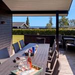 Terrasse mit Tisch und Stühlen, Blick auf Grünflächen und Meer.