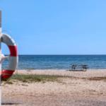 Strand mit Rettungsring, Picknicktisch und Meer unter blauem Himmel.