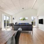 Wohnzimmer mit Sofa, Kamin und Holzboden. Fenster und Tür zur Außenterrasse.
