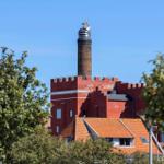 Roter Turm mit Laterne über Dachziegeln und Bäumen