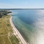 Aerial view of a coastal area with beach, water, and green landscape.
