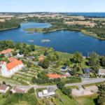 Landschaftsaufnahme mit See, Dorf und Kirche. Blick auf Küstenlandschaft mit Wiesen und Bäumen.