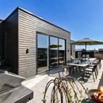Terrasse mit Grill, Tisch, Stühlen und brennendem Feuerkorb. Modernes Haus mit Glasfront.