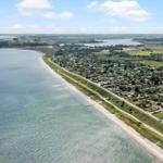 Aerial view of coastal village with houses, beach, and green fields near water.