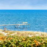 Ein hölzerner Steg mit Geländer und Sitzbank führt ins Meer.