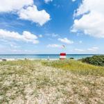 Strand mit Sanddünen, blauem Himmel und rotem Leuchtturm. Strandbad mit Sonnenschirmen.
