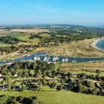 Aerial view of a coastal village with harbor, boats, and surrounding green fields.
