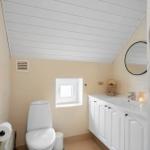 Badezimmer mit Toilette, Waschbecken und Wäschetrockner. Dachboden-Decke und kleines Fenster.