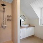 Dusche mit Duschbrause, Waschbecken mit Spiegel und Toilette in einem Dachbodenbad.