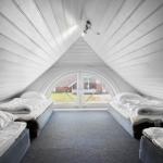 Zimmer mit drei Matratzen unter einem schrägen Dach und einer Bogenfensterfront.