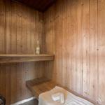 Holzsauna mit Bank, Flasche und Schwamm. Kamin mit Steinen.