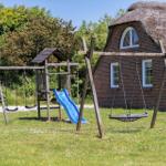 Ein Spielplatz mit Schaukel und Rutsche vor einem strohgedeckten Haus.