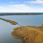 Aerial view of a wide water body with a long bridge connecting land masses under a partly cloudy sky.