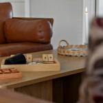 Holztisch mit Spielzeug, brauner Ledersofa und brennender Kerze im Hintergrund.