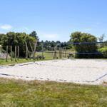Sandplatz mit Volleyballnetz und Picknicktischen im Freien.