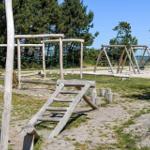 Holzspielplatz mit Klettergerüst, Schaukel und Rutsche im Freien.