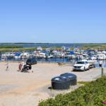 Hafen mit Booten, Parkplatz und rotem Gebäude im Vordergrund.