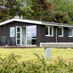 A dark brown holiday home with white trim and a terrace. A stone bench is in the foreground.