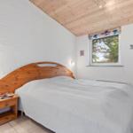 Bedroom with wooden bed, white wall, and wooden ceiling. Window with view outside.
